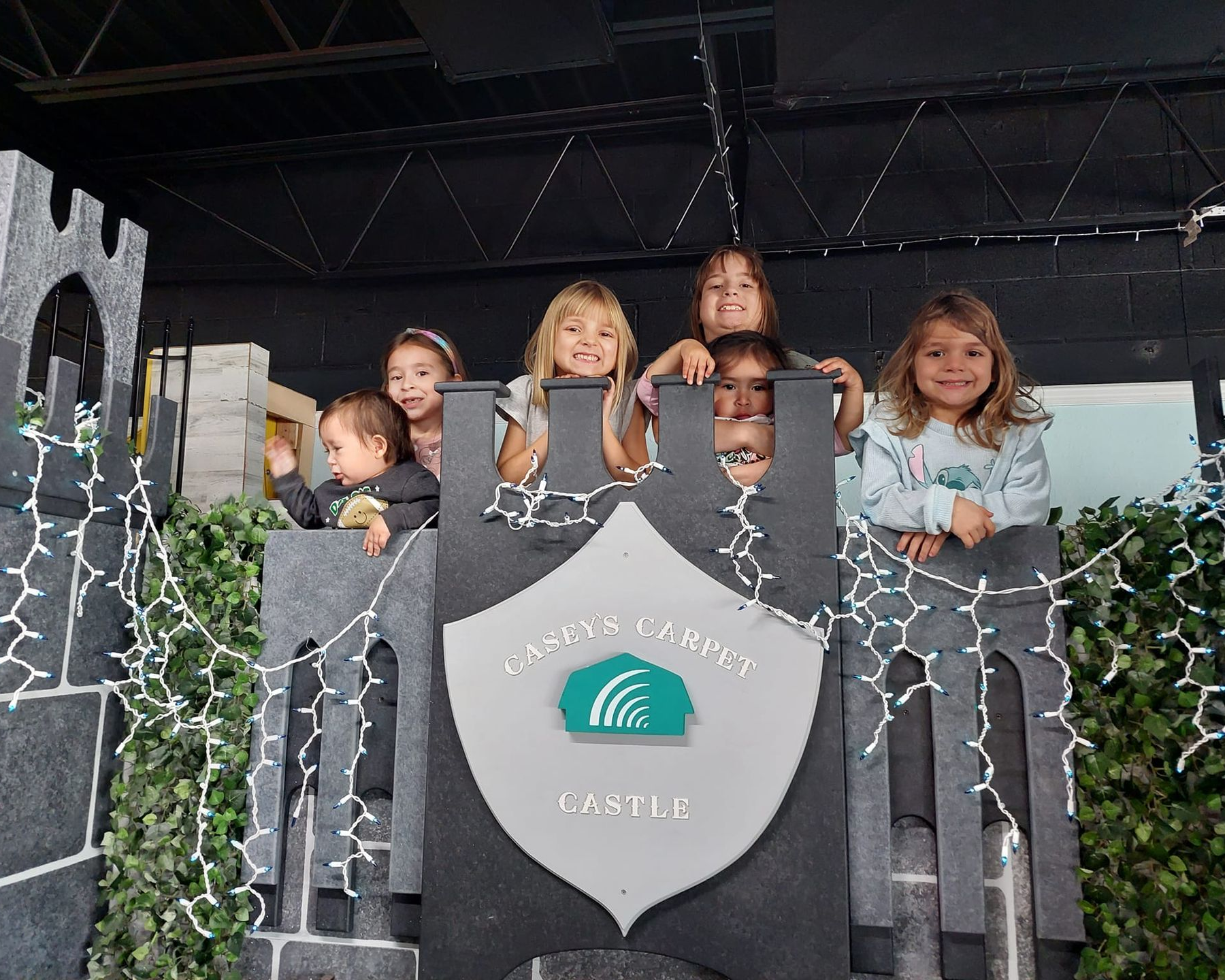 Children in a gray castle play structure, smiling and looking out.