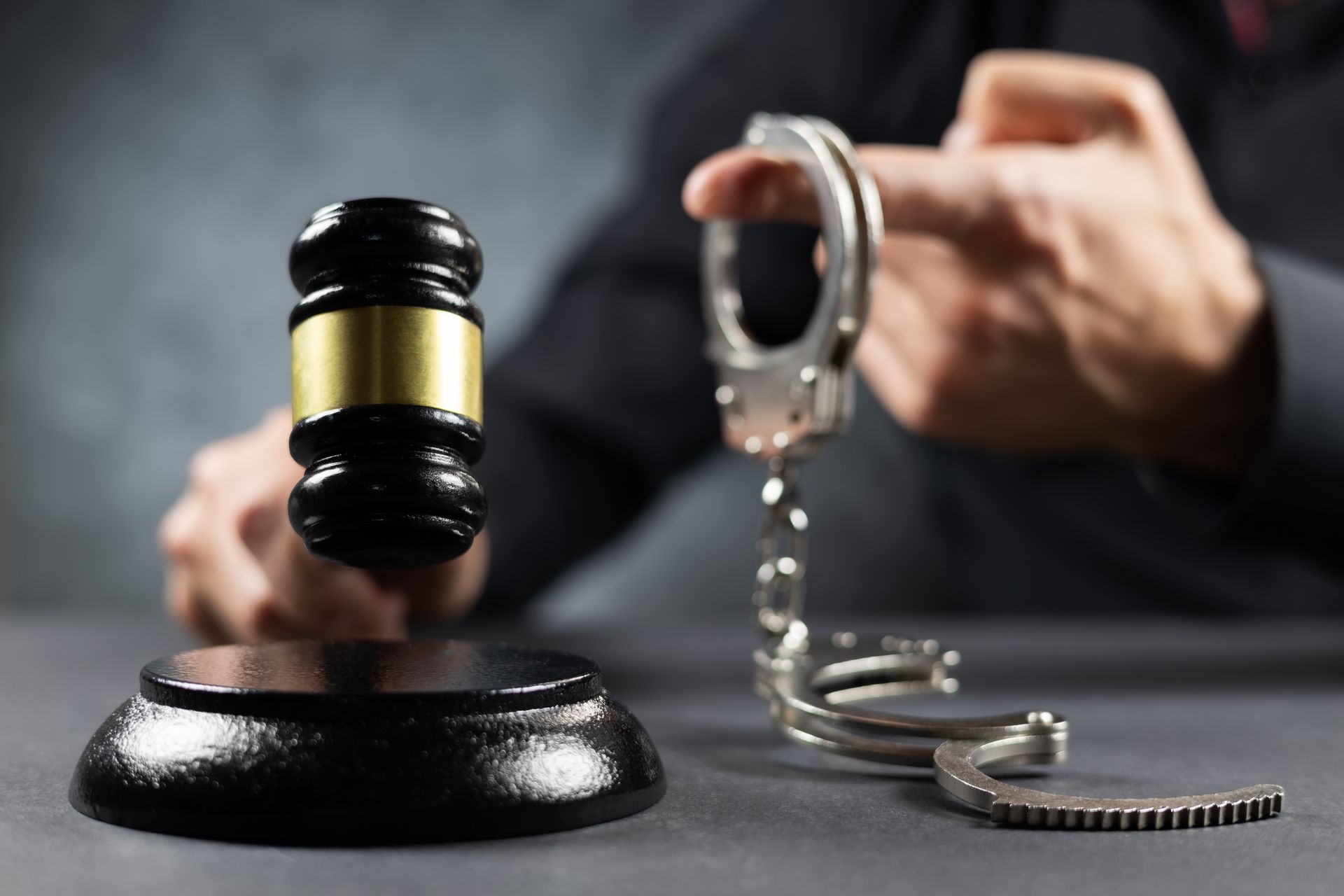 Judge's gavel held with handcuffs on a dark background.