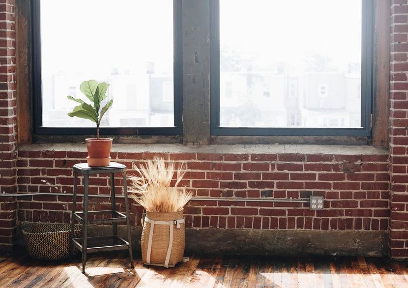 a room with a brick wall , wooden floor , and two windows .