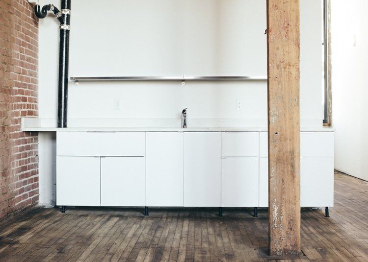 an empty kitchen with white cabinets and a wooden floor .