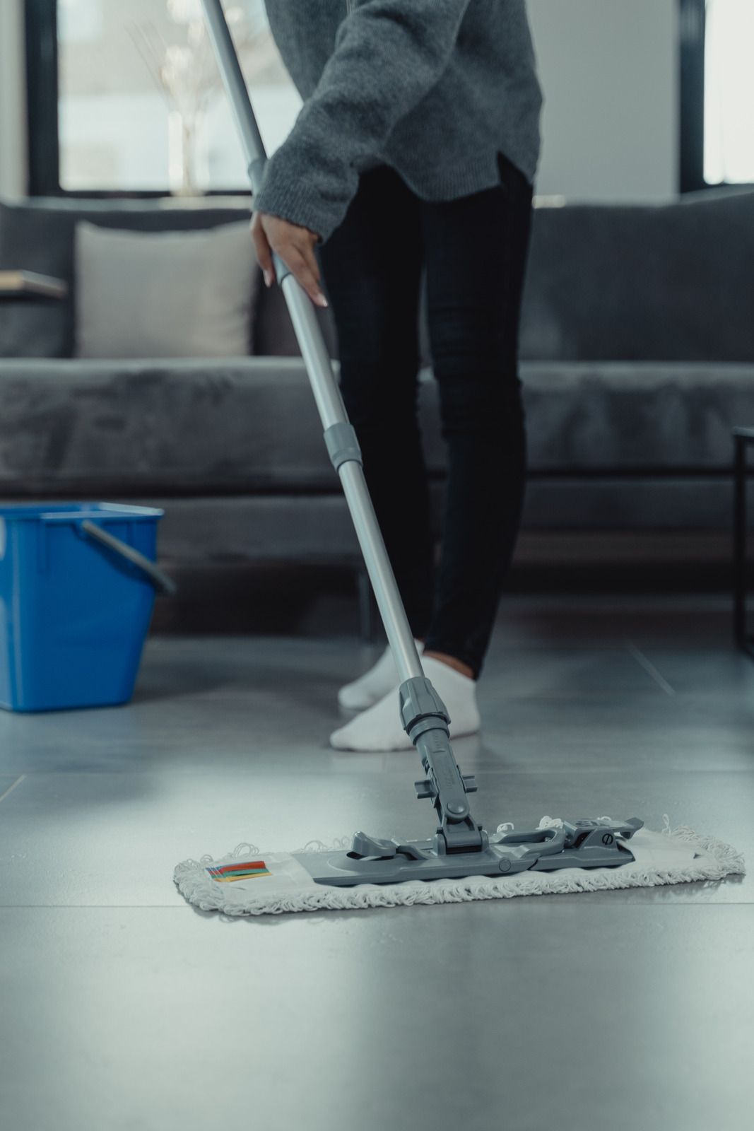 Person mopping a floor with a white flat mop in a modern room