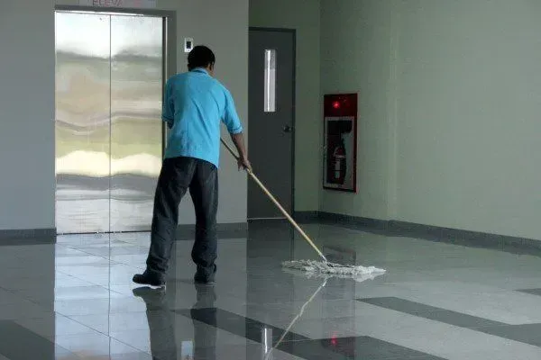 Person mopping a shiny hallway floor near an elevator in a building lobby