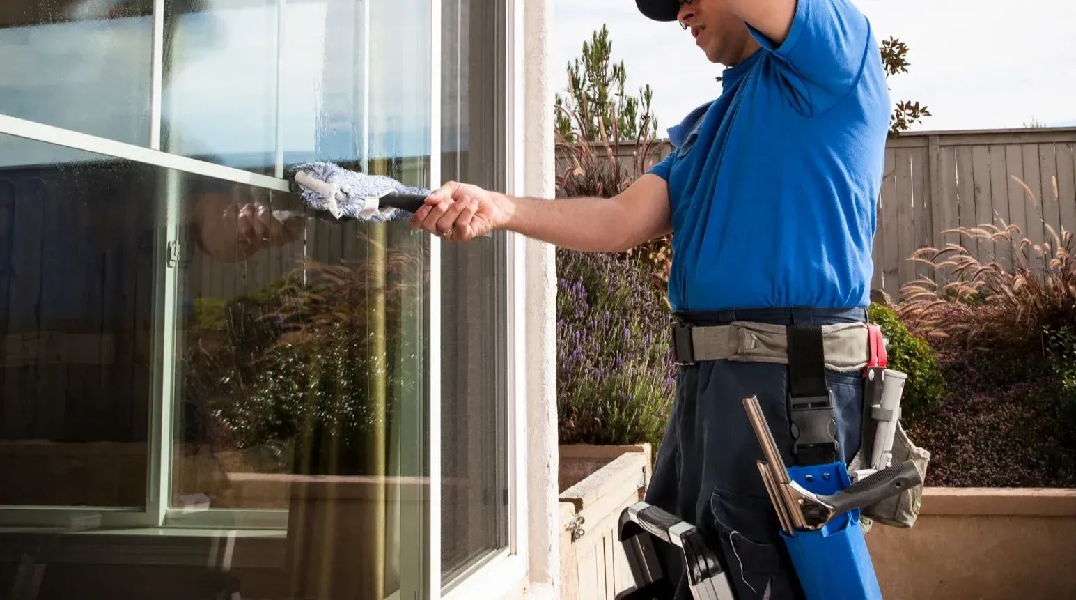 Worker in blue shirt cleaning a window with a squeegee outdoors
