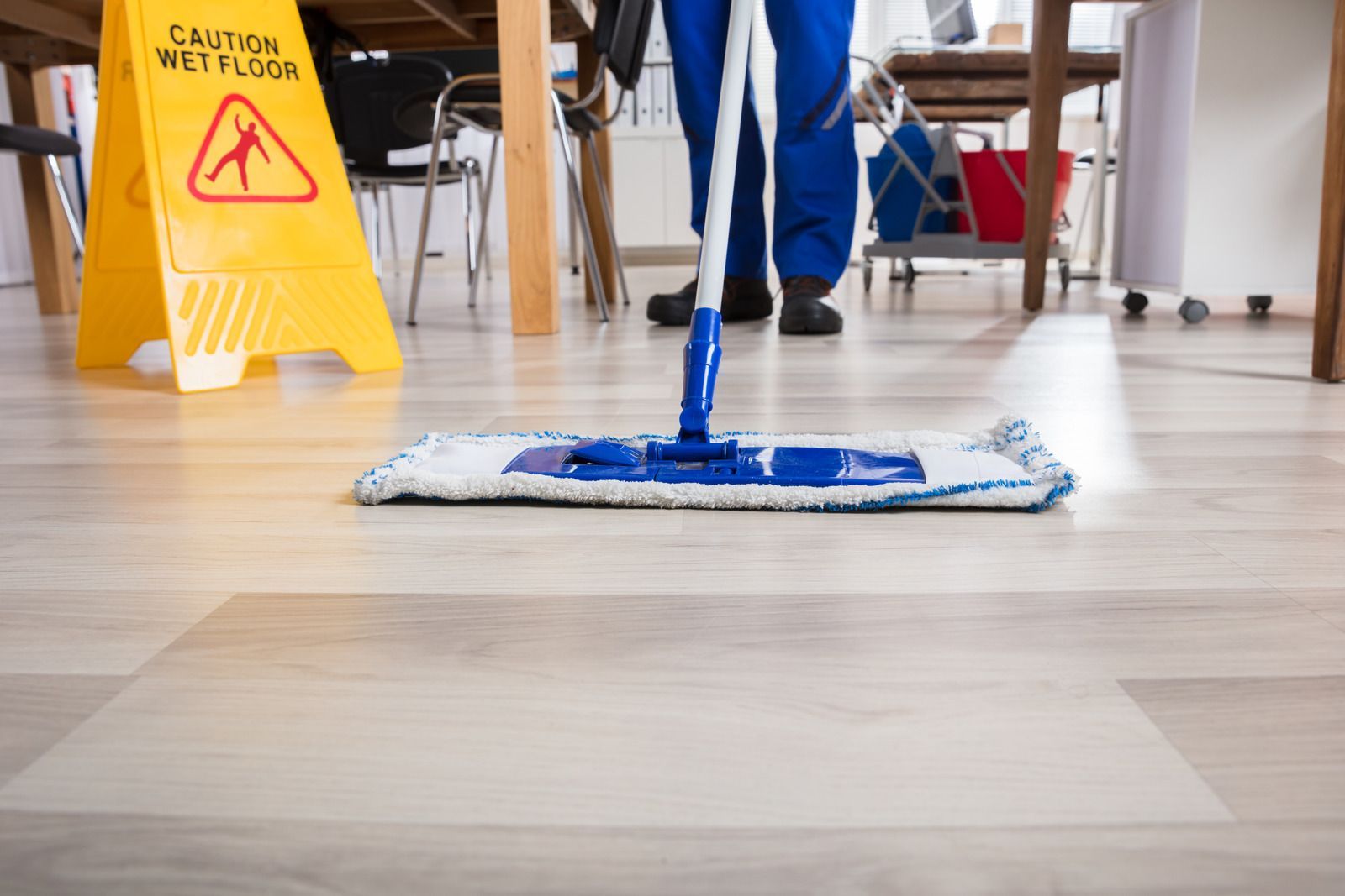 Person mopping a light wood floor in a hallway with a yellow wet floor sign nearby