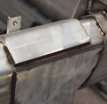 Primo piano di una scatola metallica saldata in acciaio inossidabile con piastra superiore e raccordo per tubo.