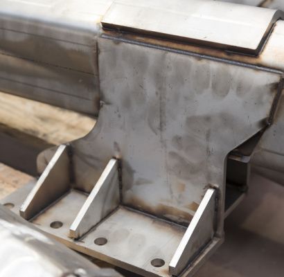 Primo piano di una giunzione di una rotaia metallica saldata, con piastre grigie, bulloni e nervature di supporto.