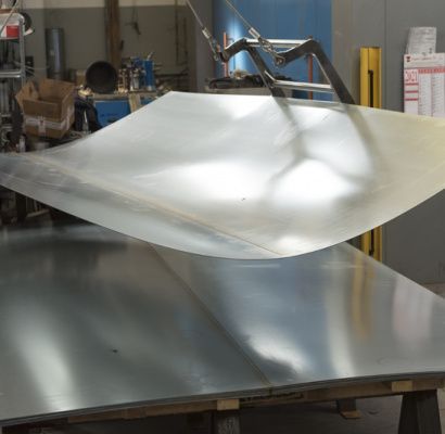 Una lastra di metallo viene sollevata da un braccio robotico in un'officina industriale.