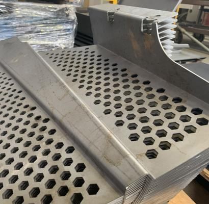 Pannelli metallici perforati impilati con fori esagonali in un ambiente di officina o fabbrica.