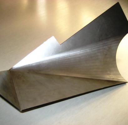 Scultura astratta in metallo, realizzata con origami, caratterizzata da pieghe angolari argentate e nere su una superficie beige.