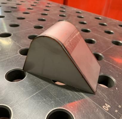 Piccolo cuneo di metallo grigio con la parte superiore rosa su un banco da lavoro in acciaio perforato.