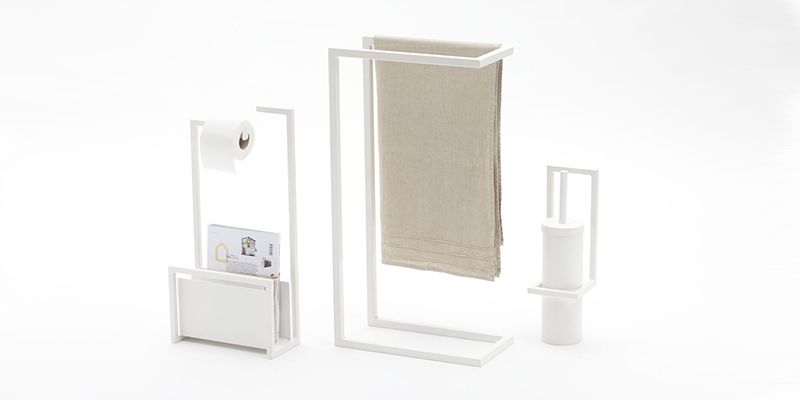 Set di accessori da bagno bianchi: supporto a parete, portasciugamani con asciugamano beige e portarotolo di carta igienica.