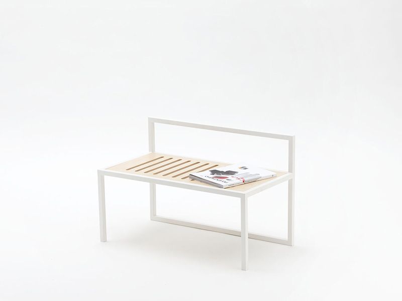 Struttura letto minimalista bianca con materasso a doghe e una rivista sopra, isolata su sfondo bianco.