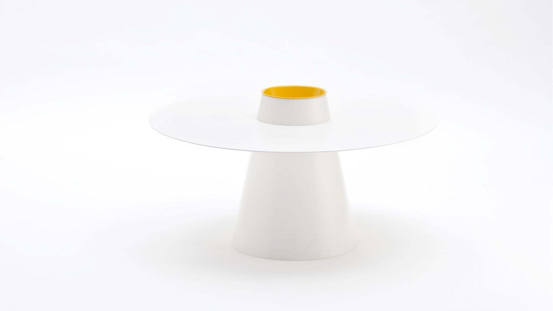 Tavolo moderno bianco con base conica e un piccolo dettaglio giallo in un monolocale minimalista.