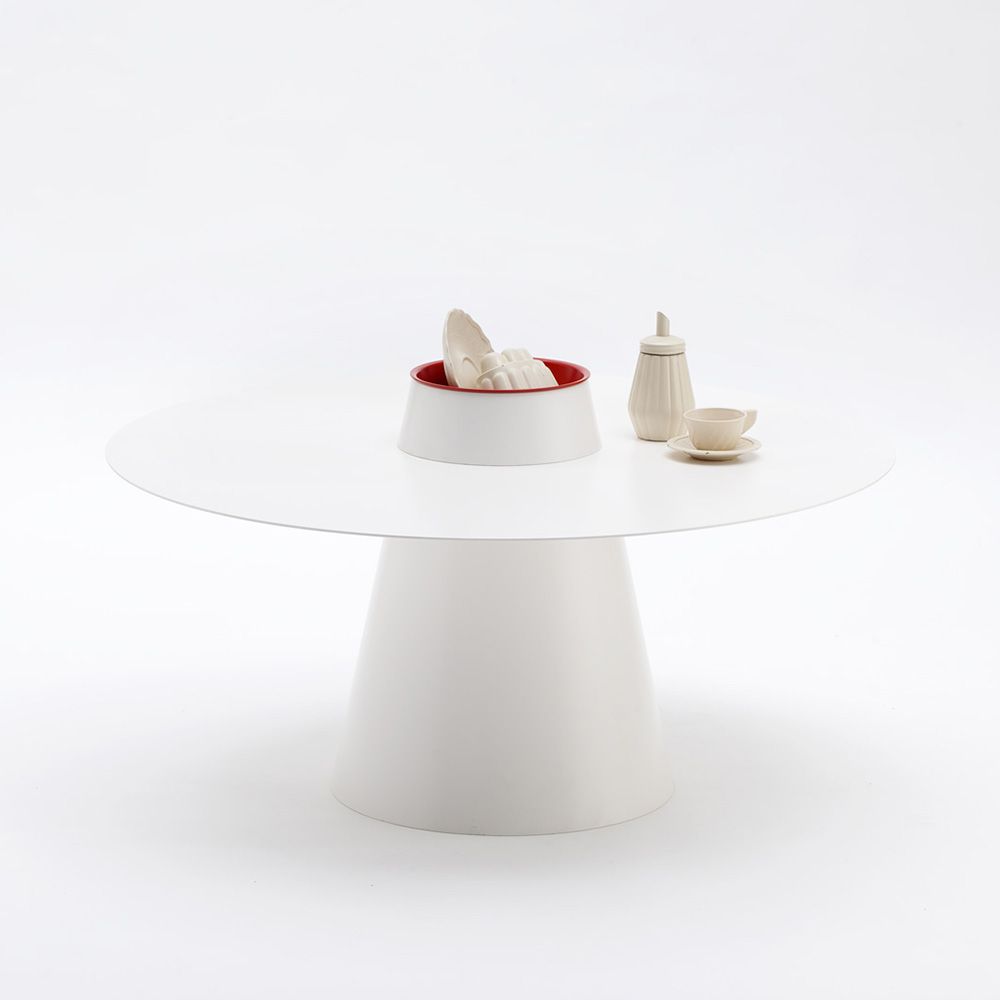 Tavolino minimalista bianco con ciotola dal bordo rosso, bottiglia e tazza su una base a piedistallo.