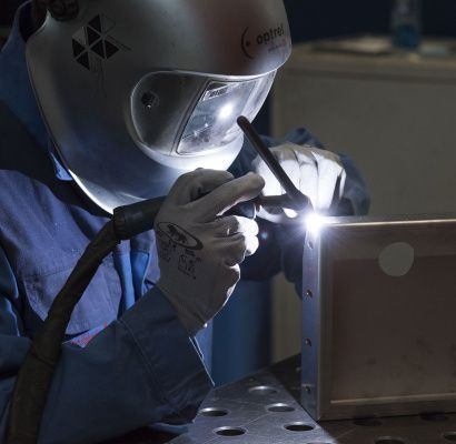 Un saldatore con casco e guanti protettivi salda metallo con scintille luminose in un'officina poco illuminata.
