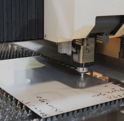 Macchina a controllo numerico (CNC) che taglia lamiere su un piano di lavoro perforato.