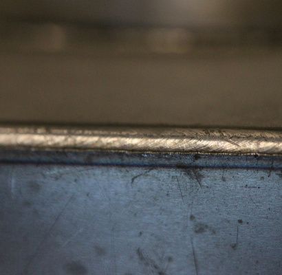 Primo piano di un bordo metallico blu graffiato con uno sfondo marrone sfocato.