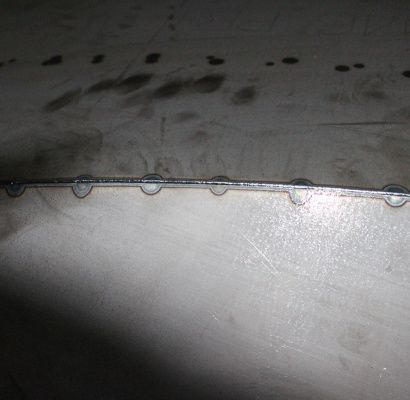 Primo piano di una saldatura metallica con elementi di fissaggio circolari su una superficie industriale grigia.