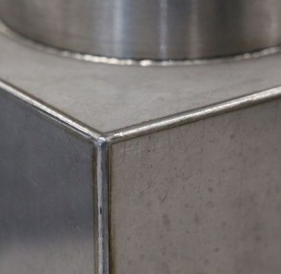 Primo piano di una giunzione angolare in metallo spazzolato con una superficie metallica cilindrica sovrastante.