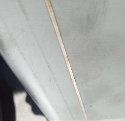 Primo piano di una parete o di un pannello bianco con una sottile linea di rifinitura verticale beige e un'ombra scura sulla sinistra.