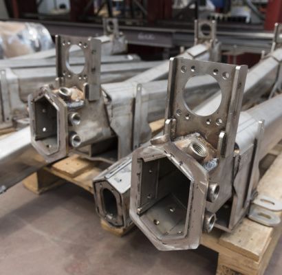 Componenti meccanici metallici impilati su pallet di legno in un'officina, che mostrano aperture esagonali.