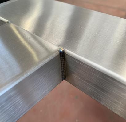 Primo piano di pannelli in metallo spazzolato che si uniscono in una giunzione con un cordone di saldatura verticale.
