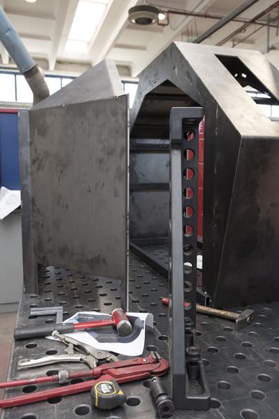 Componente di una macchina industriale su un banco da lavoro forato, con pinze rosse e una chiave inglese in primo piano.