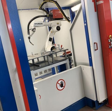 Braccio robotico industriale bianco all'interno di una struttura di sicurezza con telaio rosso e blu.