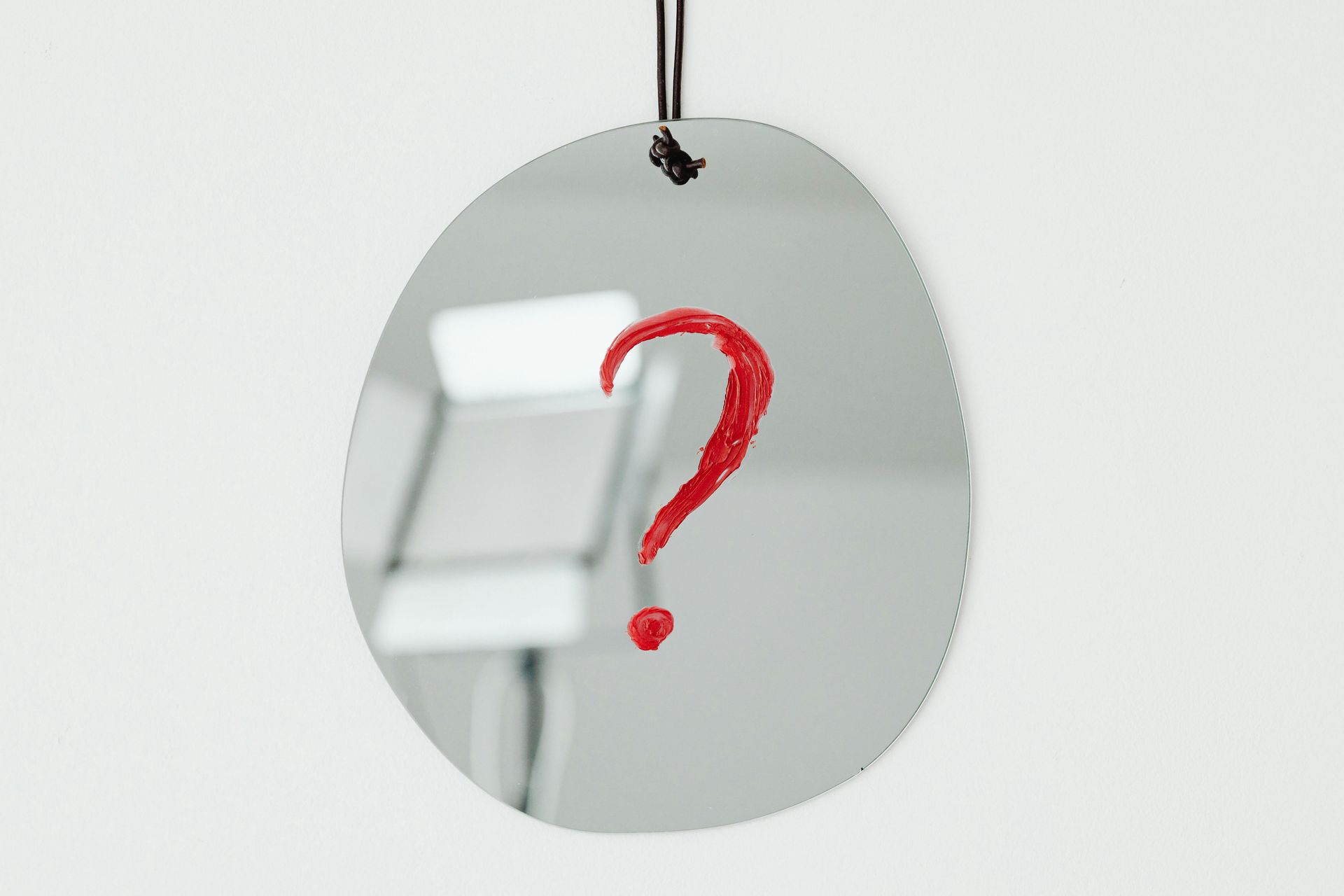 Oval mirror with red question mark, reflecting a blurred background.