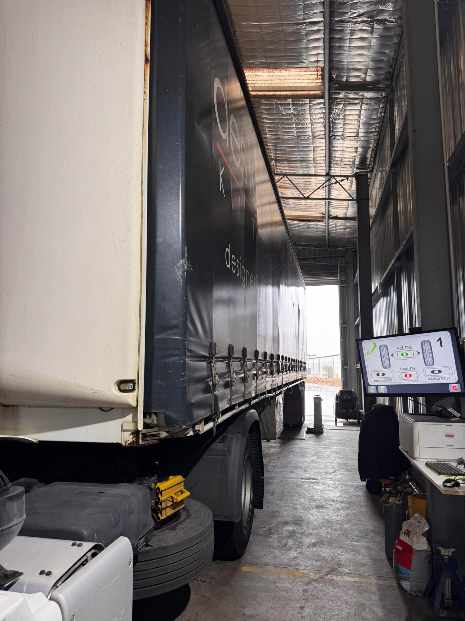 Interior of a semi-trailer loading dock with a large truck, tires, and a computer monitor in a narrow warehouse lane — B & W Commercials In Wauchope, NSW