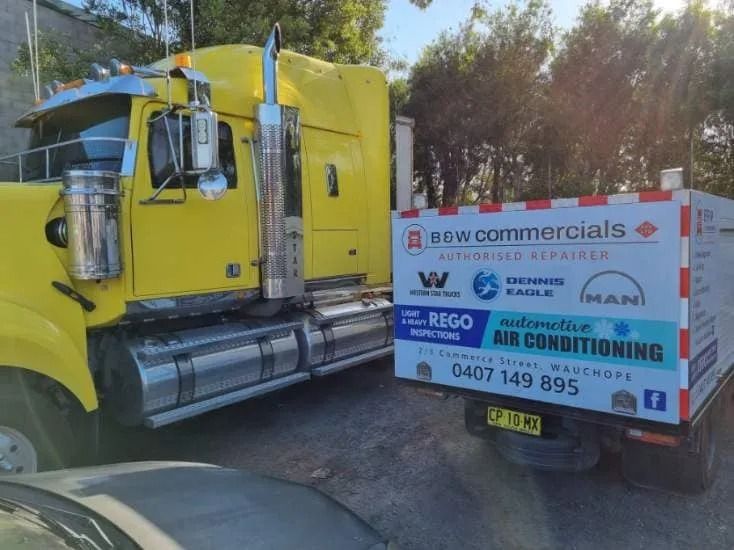 A Yellow Semi-truck Parked Next to a Service Vehicle Branded — B & W Commercials In Wauchope, NSW