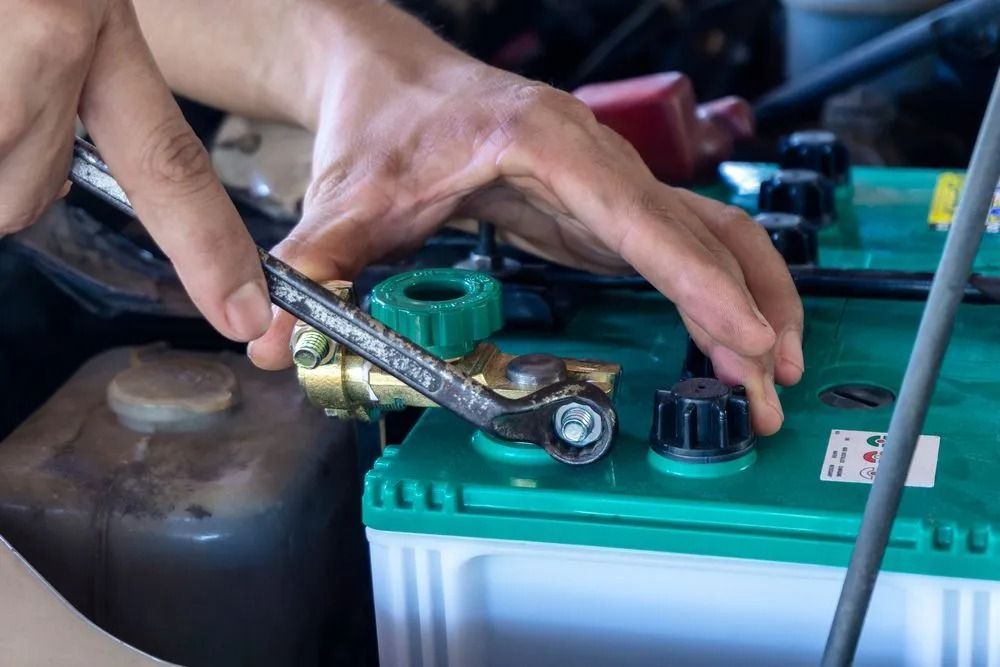 A Pair of Hands Uses a Wrench to Tighten a Terminal Connection on a Green Car — B & W Commercials In Wauchope, NSW