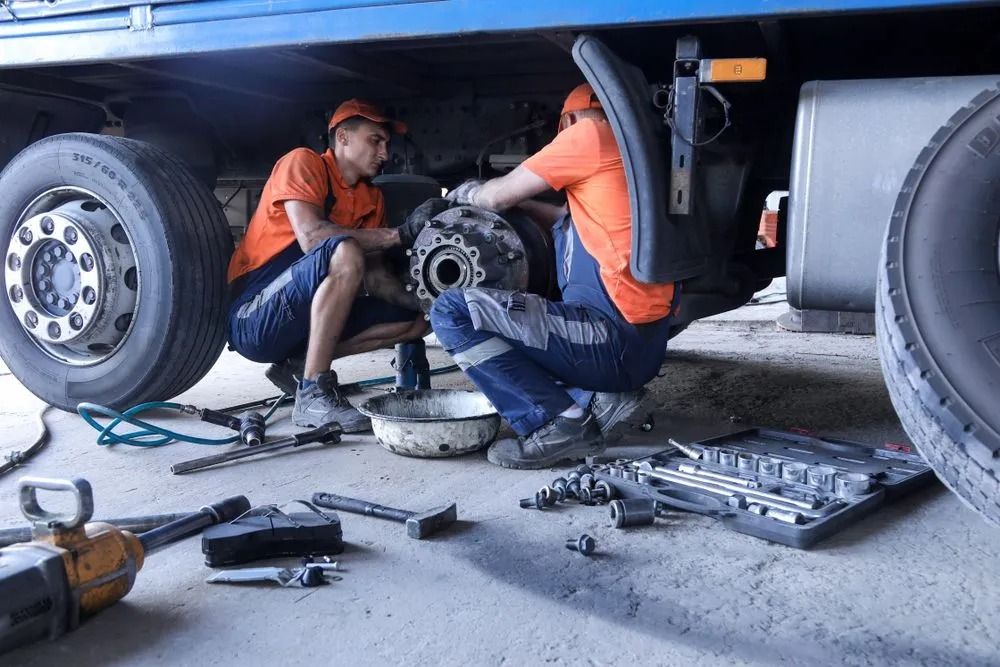 Two Mechanics in Orange Shirts and Blue Trousers Repair the Wheel Assembly — B & W Commercials In Laurieton, NSW