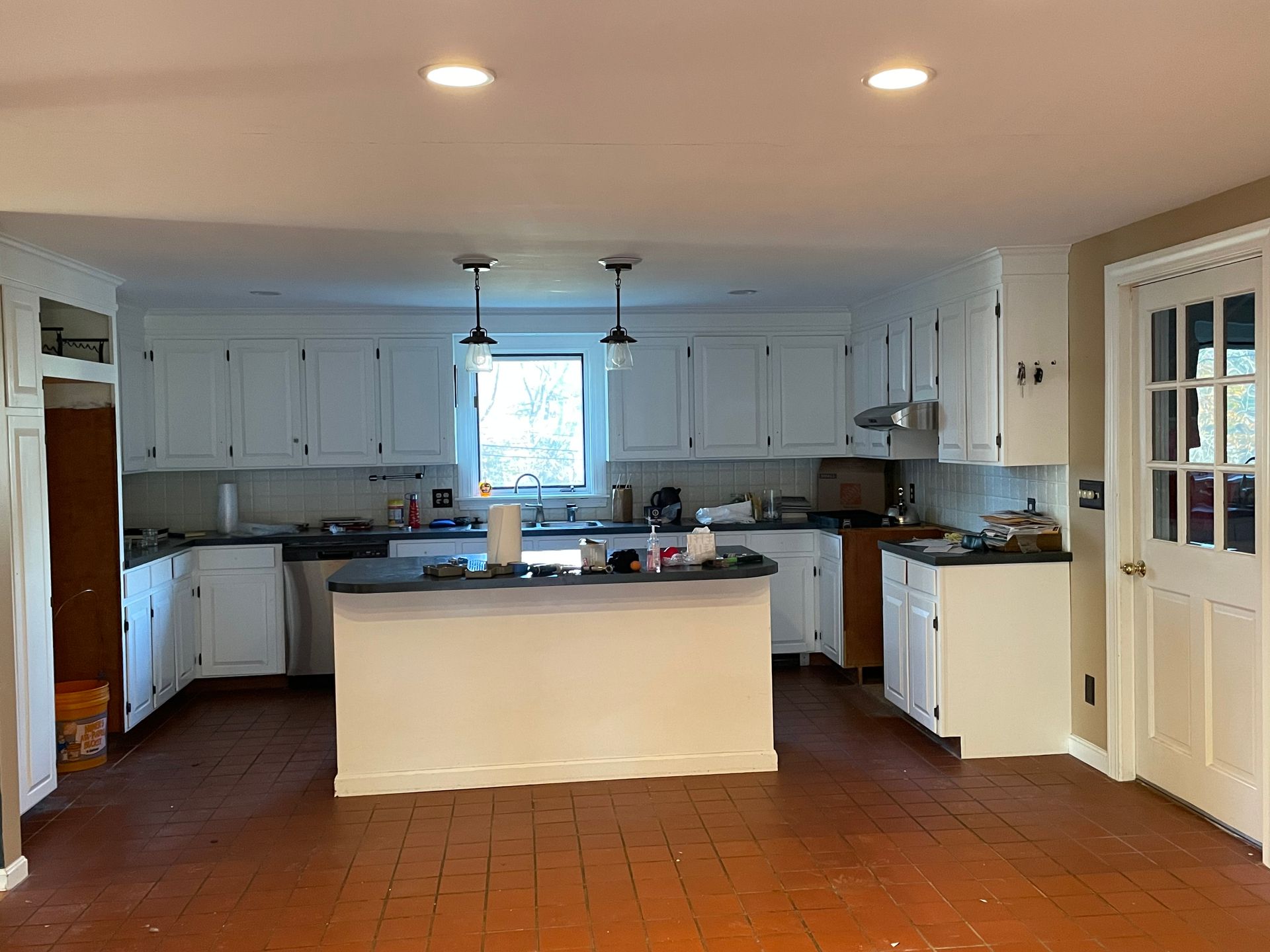 White kitchen with dark countertops, cabinets, and a central island. Brown floor.