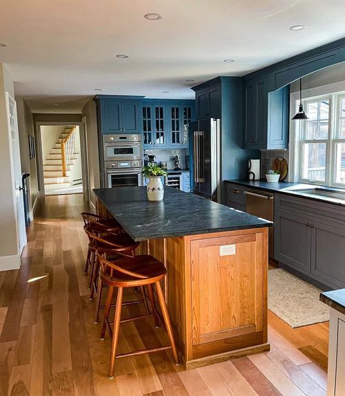 Blue and wood-toned kitchen with island and stools. Wood flooring, stairs in background.