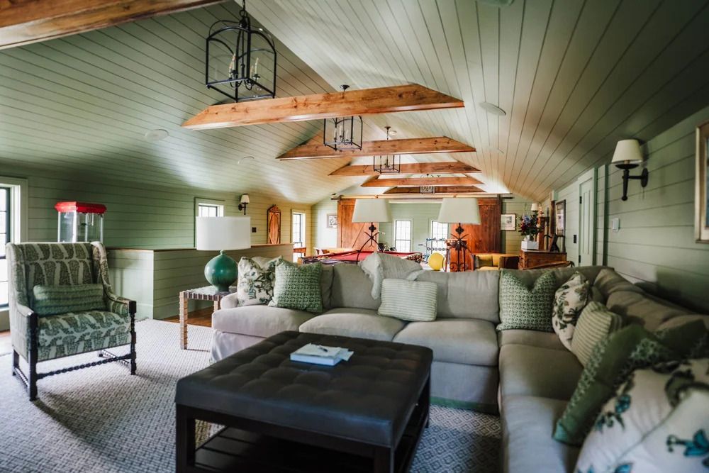 Living room with sectional sofa, armchair, ottoman, green walls, and decorative beams.