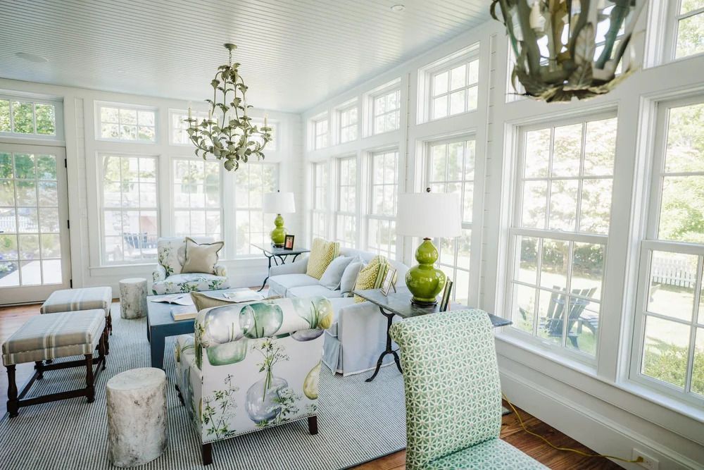 Sunroom with white trim, many windows, blue ceiling, and light-colored furniture, chandelier, and a green accent chair.