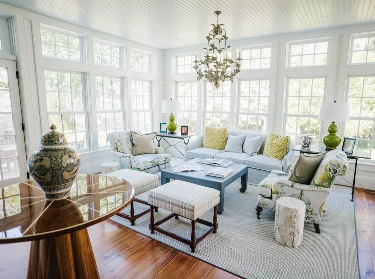 Sunroom with white walls, multiple windows, floral armchairs, gray couch, and decorative chandelier.