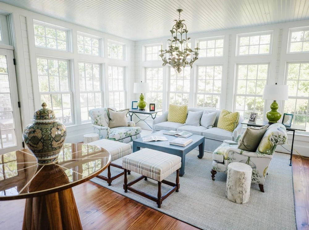 Bright sunroom with white walls, windows, chandelier, and floral furniture.