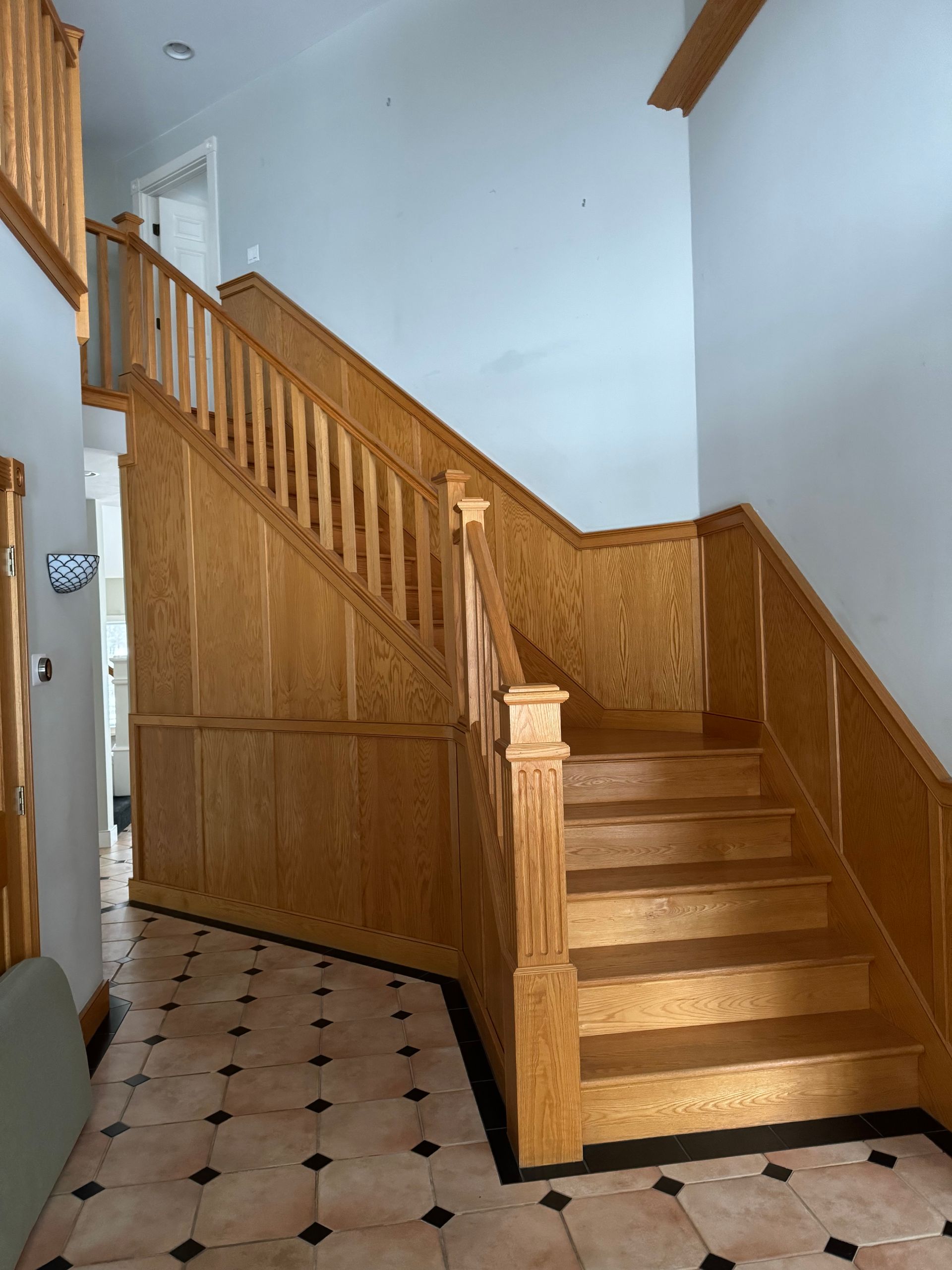 Wooden staircase with paneled walls, ascending from a tiled floor.