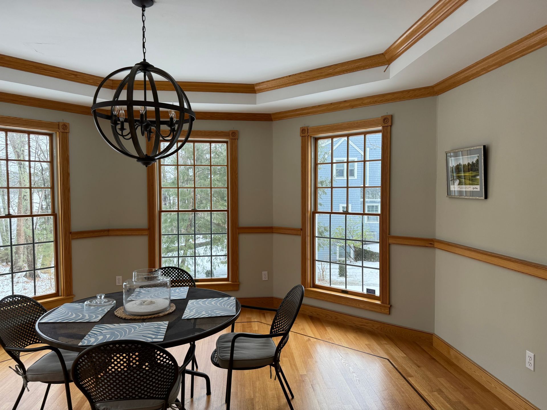 Dining room with round table, chairs, and large windows with wood trim.