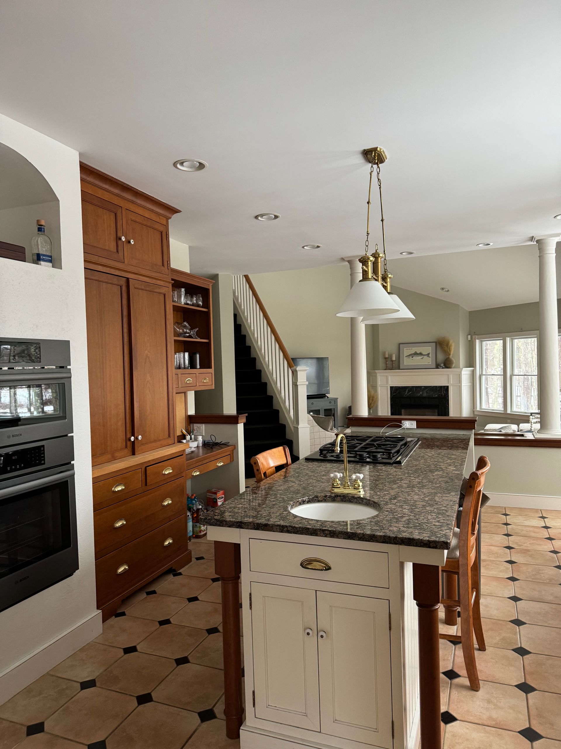 Kitchen with a large island, stove, cabinets, and a staircase in the background.