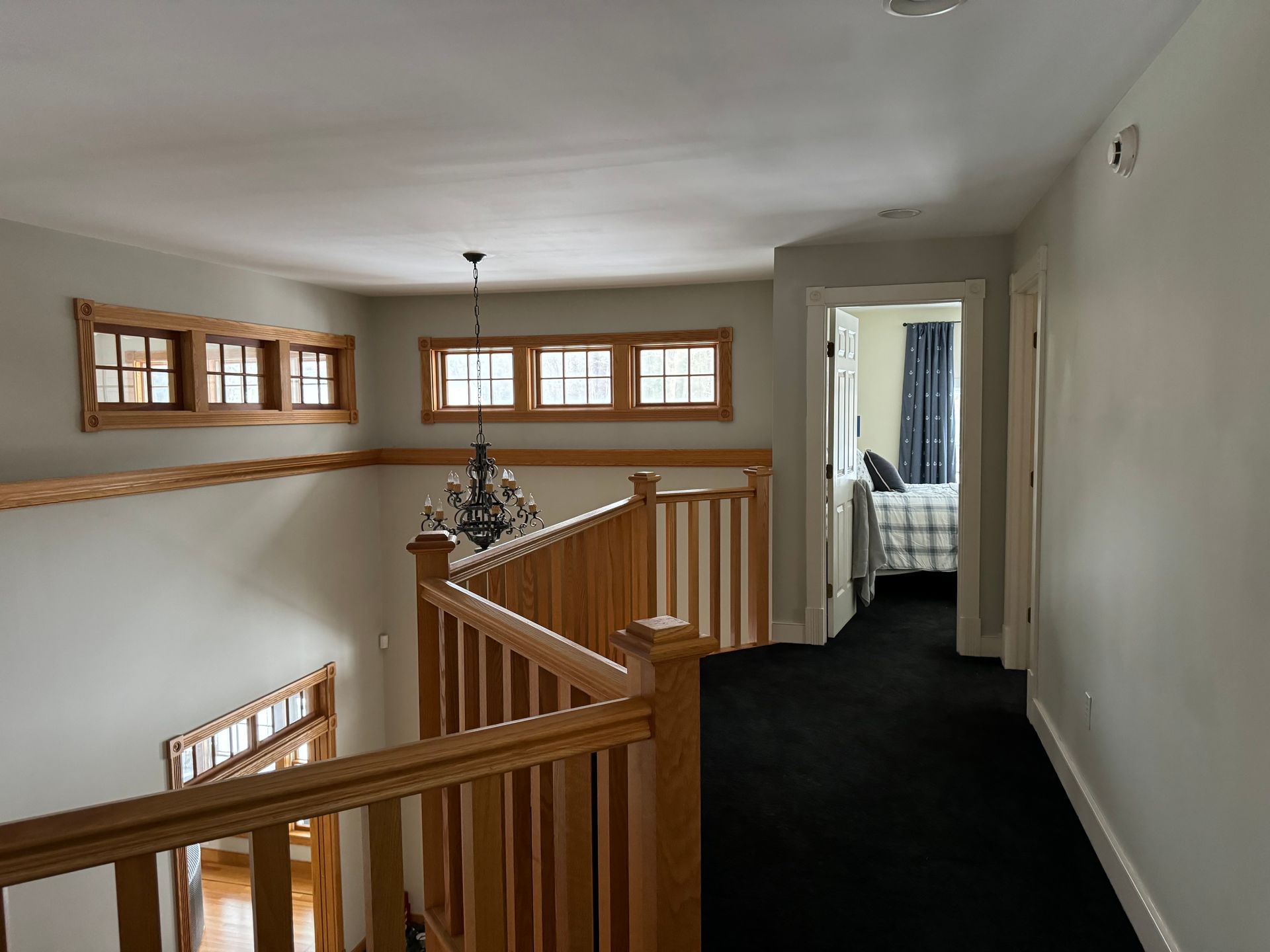 Hallway with wooden railing, windows, and a bedroom door.