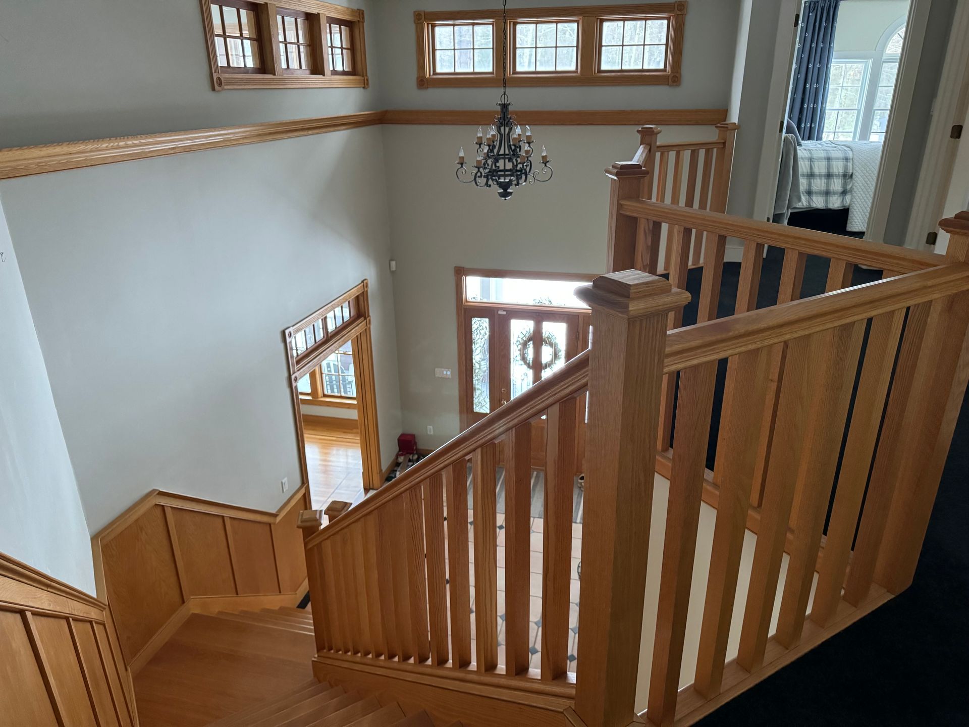 Wooden staircase leading to a front door with a wreath; chandelier hangs from ceiling.