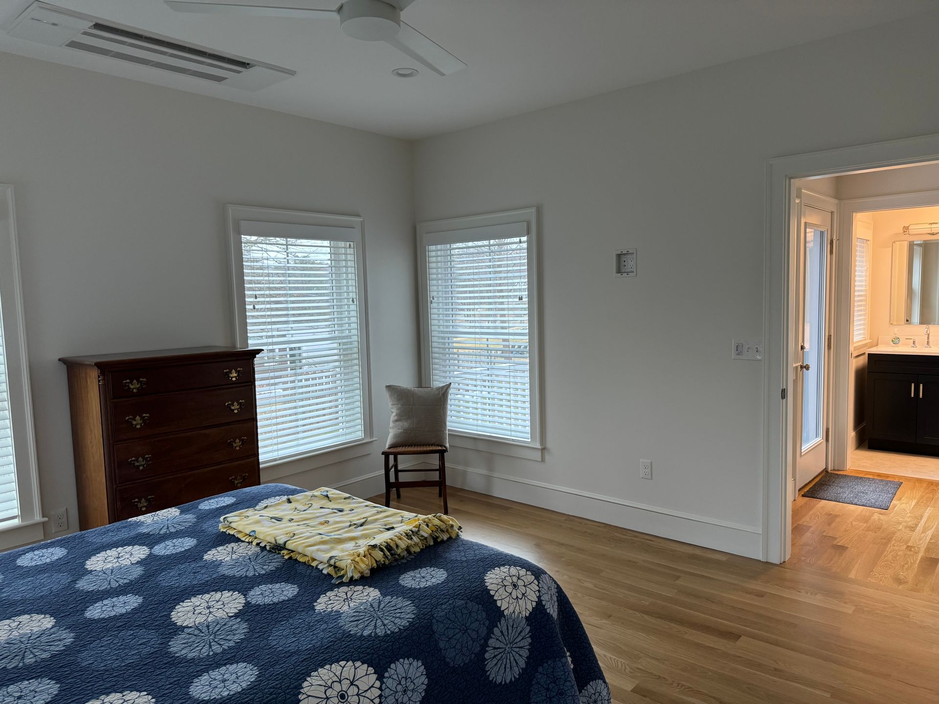 Bedroom with bed, dresser, chair, two windows with blinds, and doorway to bathroom.