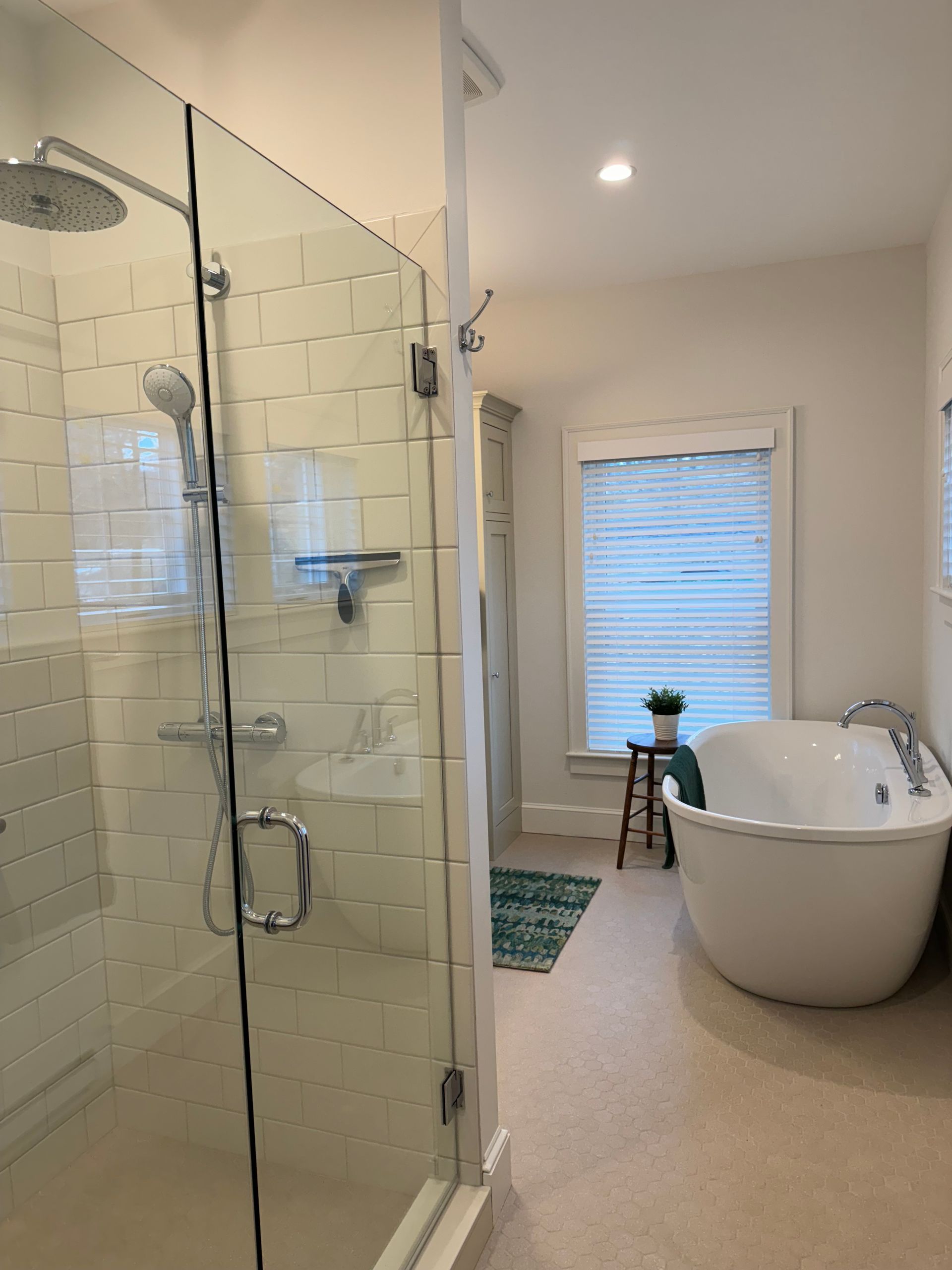 Bathroom with a glass shower, white freestanding tub, and small stool by a window.