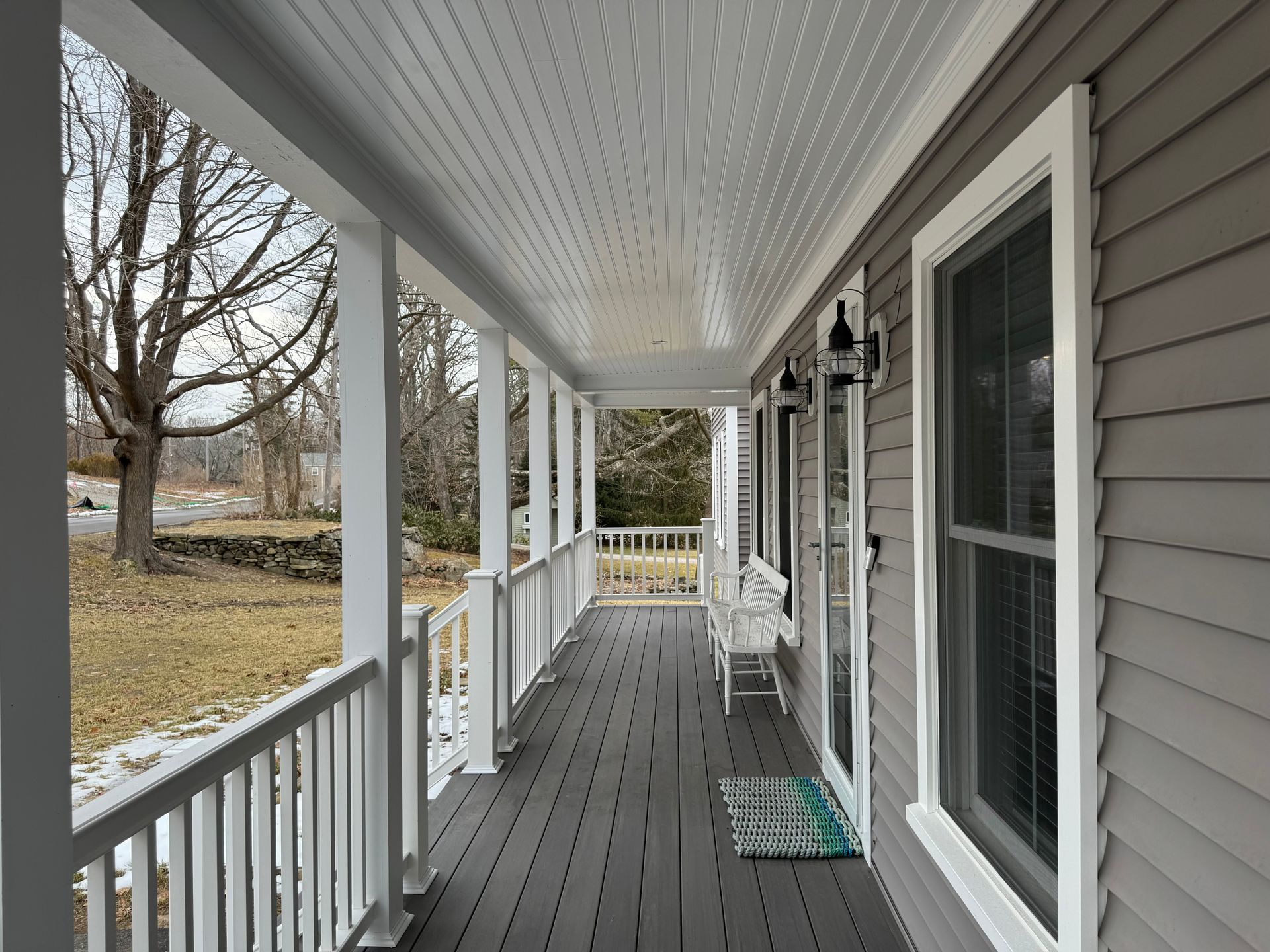 Covered porch with white columns, railings, and ceiling. Gray siding on the house, dark gray deck.