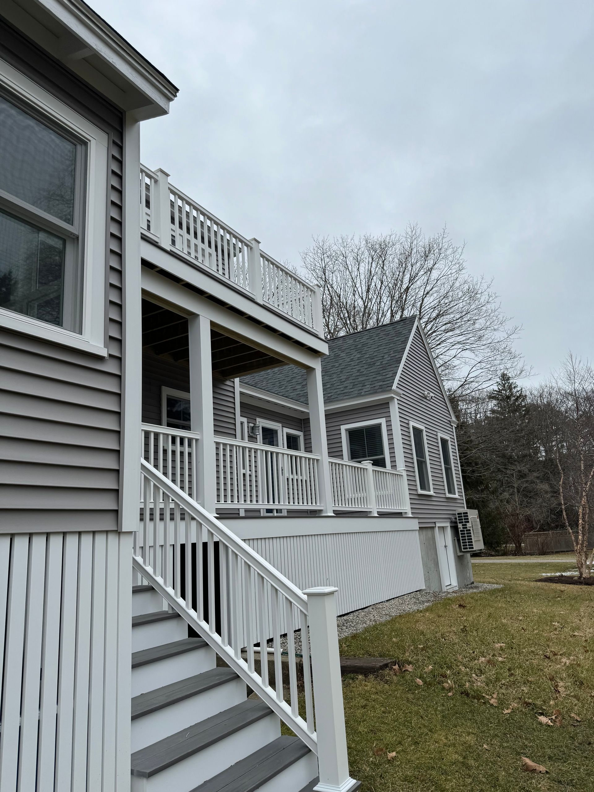 Grey and white house with deck and stairs, cloudy day.
