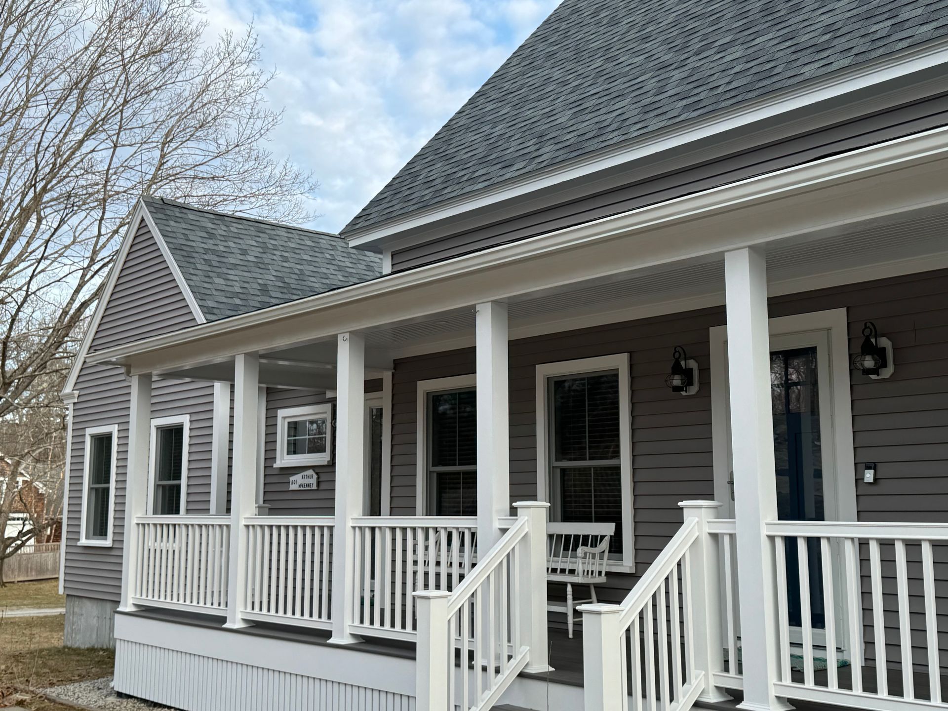 Gray house with white porch and railings. Windows, gray roof, and blue sky visible.