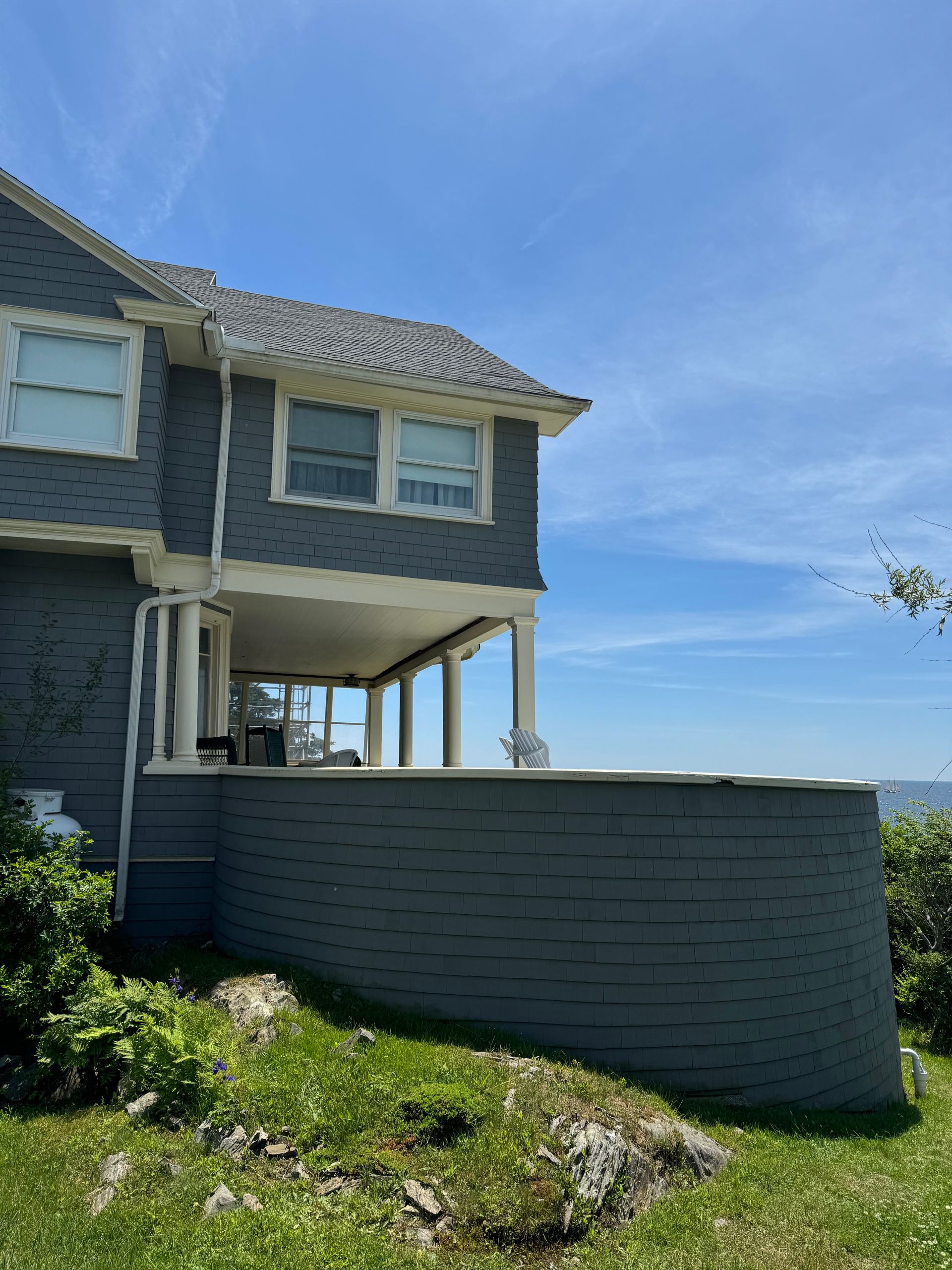 Gray house with a porch overlooking the ocean, under a blue sky.